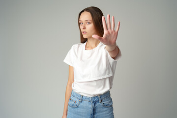 Portrait of a young woman standing with outstretched hand showing stop gesture on gray background