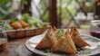A tempting plate of Indian samosas, crispy and golden brown, filled with a savory mixture of spiced potatoes, peas, and aromatic herbs, served with tangy tamarind chutney for dipping.