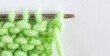 Close-up view of process of hand knitting spring green wool scarf on metal knitting needle. Empty space for text on white background. Flat lay, copy space, macro, mock up