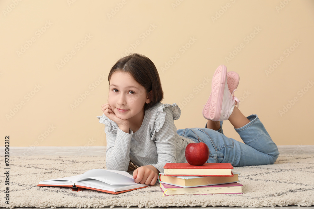 Little girl reading book near beige wall. Children's Day celebration