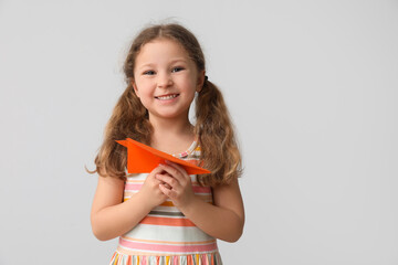 Wall Mural - Little girl with paper plane on light background. Children's Day celebration