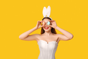 Poster - Sexy smiling young woman in bunny ears with Easter eggs on yellow background