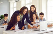 © Studio Romantic - Group of high school students and classmates sitting in the classroom with male friendly smiling teacher and looking at the laptop monitor screen. Education and back to school concept.