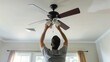 © Borin - An electrician installing a ceiling fan in a living room.