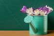 Crocuses in a watering can standing on a table in front of a chalkboard