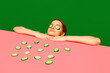 © master1305 - Spa and relaxation. Young woman peeking over table with cucumber slices on face, homemade refreshing mask against green background. Concept of food pop art photography, creativity, quirky style