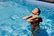 © SHOTPRIME STUDIO - Happy woman swimming in pool in red swimsuit with loose long hair in sunshine, skin protection with sunscreen, concept of relaxing on vacation in tropical climate.