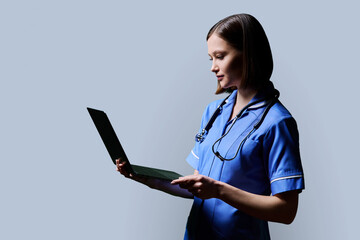 Female nurse using laptop, profile view on gray studio background