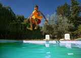 Fototapeta  - Sunny poolside fun with jumping teen boy captured in motion