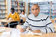 © JackF - Young adult man working with books, finding information at library
