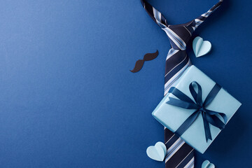 Celebrating Dad: Overhead shot of a neatly wrapped gift, bowtie, and hearts, all arranged on a bold blue background with ample space for messages