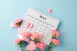 Mother's Day blue serenity: An overhead view of May's calendar, pink carnations, and hearts on a tranquil blue backdrop, with space for expressions of affection