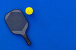 © Mike Orlov - Pickleball tennis racket on the court. Blue background with copy space. Sport court and ball.