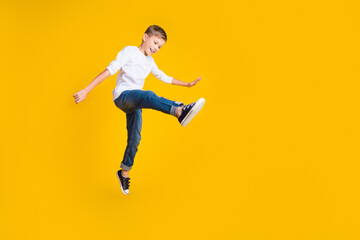 Wall Mural - Full length photo of funky good mood kid dressed white shirt jumping high walking empty space isolated yellow color background