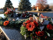 A Wreath Of Red Flowers Sits On A Tombstone. The Flowers Are Surrounded By Greenery And Are Arranged In A Way That Creates A Sense Of Peace And Serenity. The Tombstone Itself Is A Simple