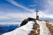 Ein Wanderer lehnt am Hochgern Gipfelkreuz mit beeindruckende Aussicht über die Chiemgauer Berge in Bayern Deutschland