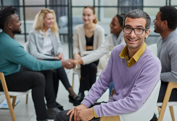 Wall Mural - A happy young businessman, in a purple sweater, sits against the background of his colleagues