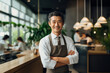 Mature Asian businessman in white shirt and brown apron with arms crossed in modern restaurant