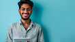 Happy young Indian man using a digital tablet isolated against blue background, smiling and happy.