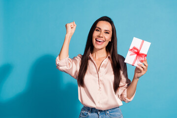 Sticker - Portrait of overjoyed girl with long hairstyle wear silk blouse hold present box scream yeah fist up isolated on blue color background