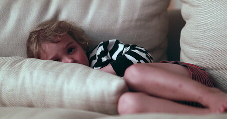 Wall Mural - Child watching TV screen while laid in living-room sofa