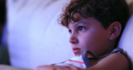 Wall Mural - Child watching TV screen, casual candid young boy seated at living-room sofa