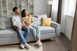 © Home-stock - Relaxed hindu couple resting on sofa, chilling on comfy couch, cuddling and looking out window in living room, free space, full length shot