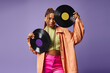 stylish african american woman in her 20s with dreadlocks posing with vinyl discs on purple backdrop
