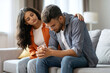 © Home-stock - Apologize at home. Indian woman calms offended guy, support and caring, sitting together on sofa in room interior. Bad news reaction and crisis