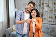 © Home-stock - Satisfied young indian spouses show keys at own flat in living room, enjoy moving, buying new home, renting house together, copy space