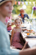 © Halfpoint - Portrait of a beautiful little girl sitting at table eating grilled food outdoors. Girl at family garden party.