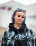 Fototapeta Sawanna - Young woman with colorfull blue hair, piercings and sunglasses posing. Wearing flannel and hoodie. Urban background.