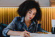 © InsideCreativeHouse - Concentrated young african woman studying in a cozy cafe. Female student freelancer university college learner doing homework remotely, planning projects, doing startups, completing course