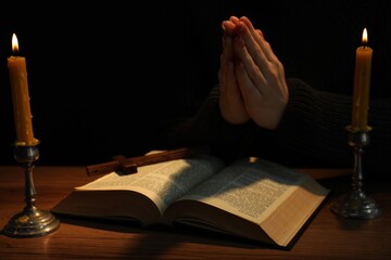 Woman praying at table with burning candles and Bible, closeup