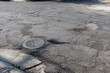 Undulating asphalt with patch layers crumbling, manhole drain creative copy space for transportation theme, infrastructure, horizontal aspect