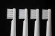 Four white plastic toothbrushes on a black background, closeup