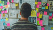 Project Planning and Brainstorming with Sticky Notes. Back view of a person contemplating a wall filled with colorful sticky notes and project planning materials during a brainstorming session.