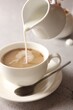 © New Africa - Pouring milk into cup with coffee on light grey textured table, closeup
