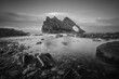 Black and white landscape of natural sea arch and stones in the foreground covered with water. Famous rock formation on the Moray Coast, Scottish Highlands, Scotland. Bow Fiddle Rock, long exposure.
