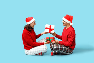 Poster - Happy young couple in Christmas pajamas and with gifts sitting against blue background