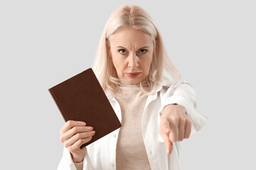 Mature woman with Holy Bible pointing at viewer on light background, closeup. Accusation concept