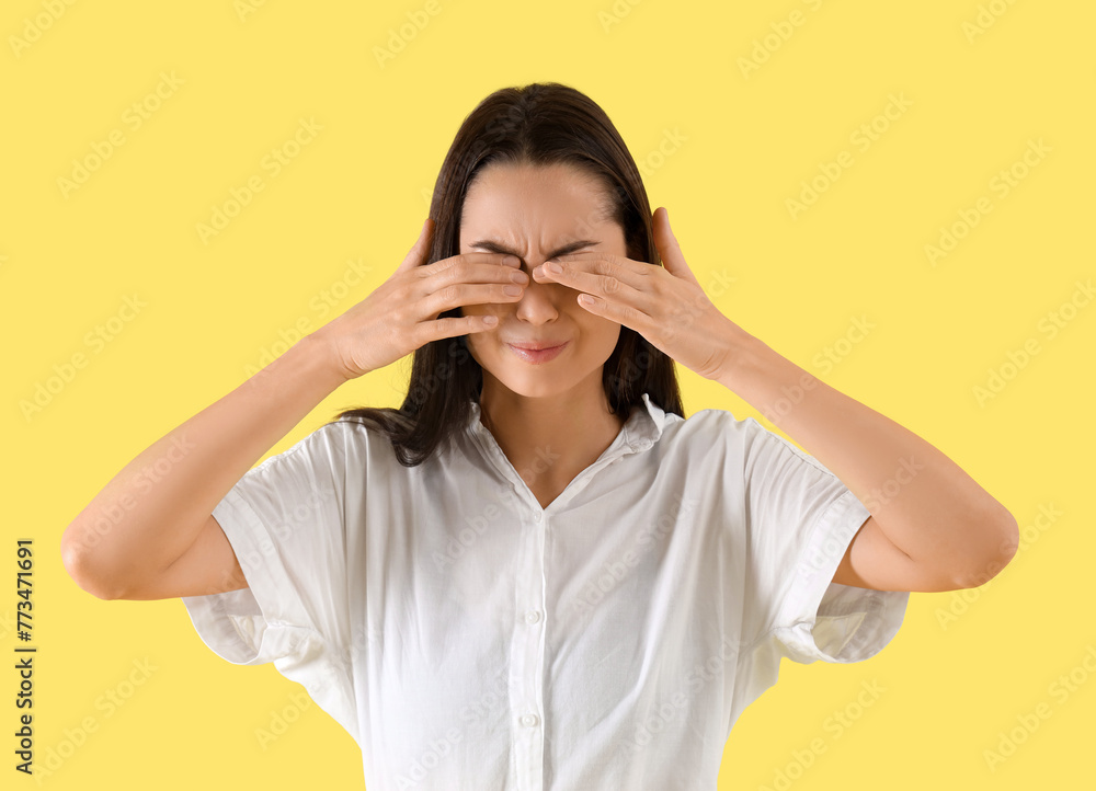 Young woman suffering from headache on yellow background