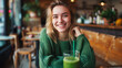 cute girl in a green jacket drinks a green smoothie while sitting in a cafe. Healthy eating concept.