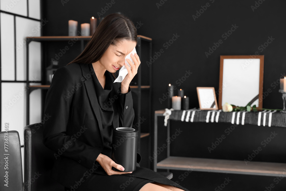 Grieving young woman with mortuary urn crying at funeral