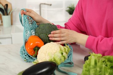 Wall Mural - Woman taking vegetables out from string bag at light marble table, closeup