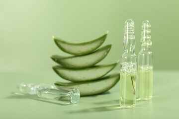 Skincare ampoules with extract of aloe vera and cut leaves on pale green background, closeup