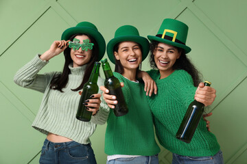 Wall Mural - Beautiful young women in leprechaun hats with bottles of beer on green background. St. Patrick's Day celebration