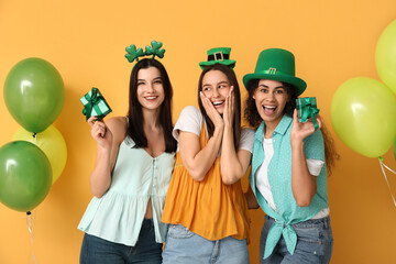 Poster - Beautiful young women with gift boxes and air balloons on yellow background. St. Patrick's Day celebration