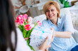 Close up photo of smiling caring grownup millennial daughter present gift and flowers to mature mom on mothers day. Birthday, Mothers day, women's day, retired, family, relation, motherhood.