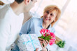 Close up image of adult son giving present and flowers when greeting to his mature mother at home. Birthday, Mother's day, women day, retired, family, relation.